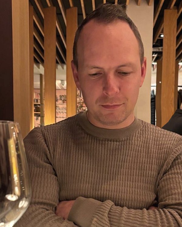 De maker van Denckh aan tafel in een restaurant, armen over elkaar, kijkend naar de menukaart.